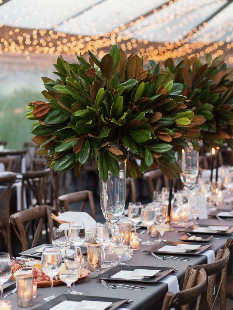 elegant tall wedding centerpieces with magnolia leaves in glass vases down the center of long banquet table