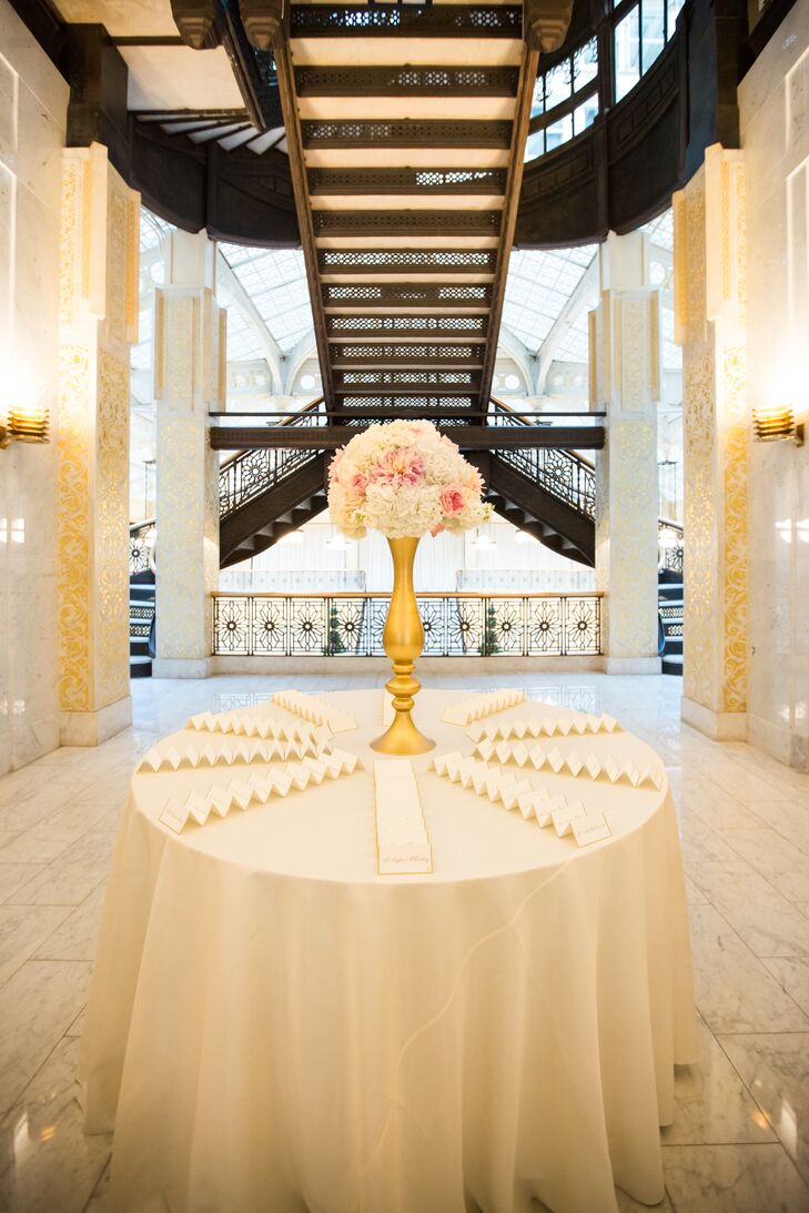 Guests found their seats at a simple escort card display that incorporated gilded cards and a lush arrangement of blush and white blooms.