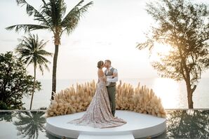 Bride in A-Line Gown With Champagne Underlay, Crown Kissing Groom in Gray Suit on Platform, Pampas Grass and Ocean Views