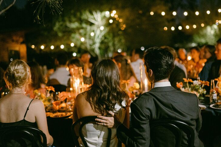 Bride and Groom From Behind the Head Table, String Lights at Nighttime Reception
