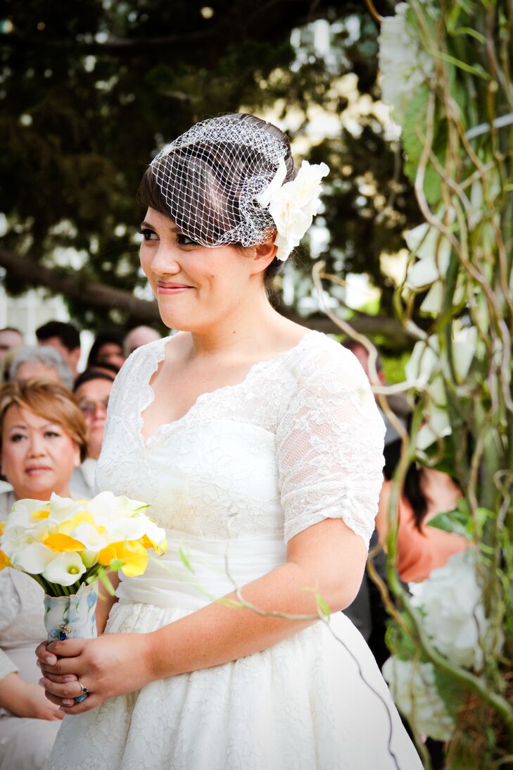 Brandy walked down the aisle wearing an ivory birdcage wedding veil with a fabric flower pinned to the side of her updo. She wore an ivory wedding dress accented with lace, and held a canary yellow and ivory calla lily bouquet.