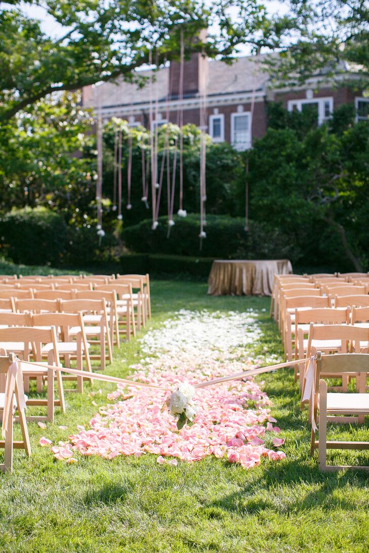 Their outdoor ceremony was the picture of summer with bright flowers and soft cascading details. Pink and white ombre flower petals filled the aisle between rows of wooden folding chairs. A bunch of white hydrangeas on pink ribbons marked the entrance, adding a more natural feel to the design.