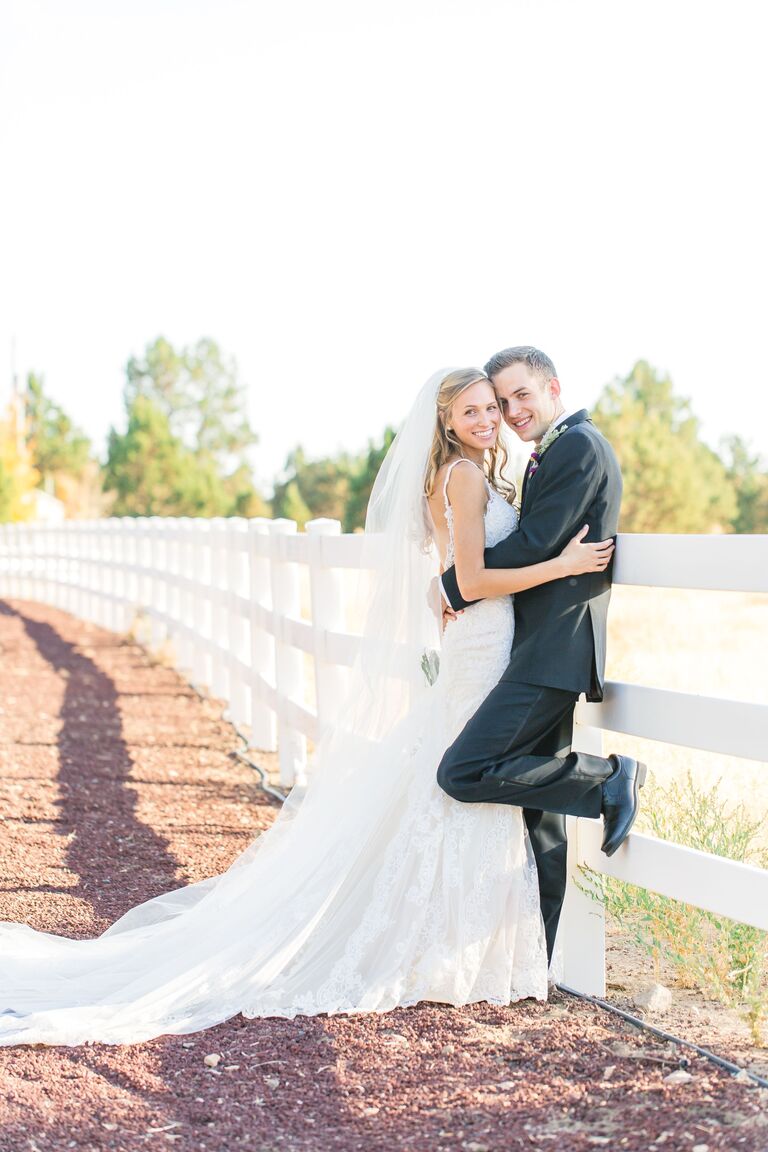 bride and groom posing by white fence