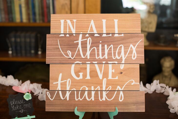 Wedding signs made of wood panels decorated the day, giving the elegant occasion a bit of a rustic edge. This sign had white writing that read "In all things give thanks," perched up by a mint green stand.