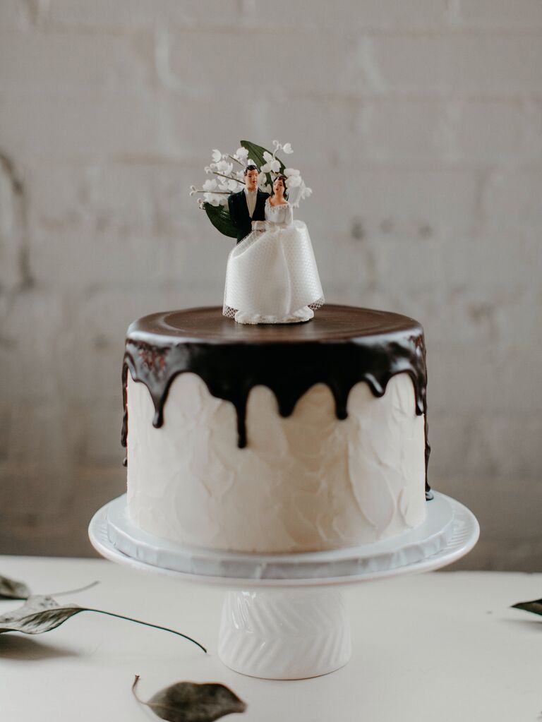 one tier wedding cake with white buttercream frosting, chocolate drip icing and vintage bride and groom topper