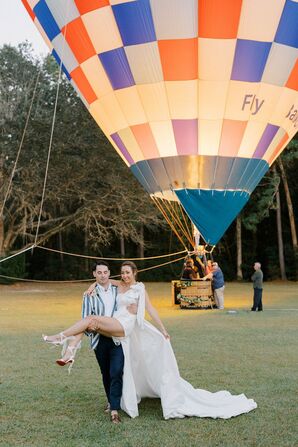 Groom in Seersucker Carrying Bride in Romper With Train Away From Hot Air Balloon