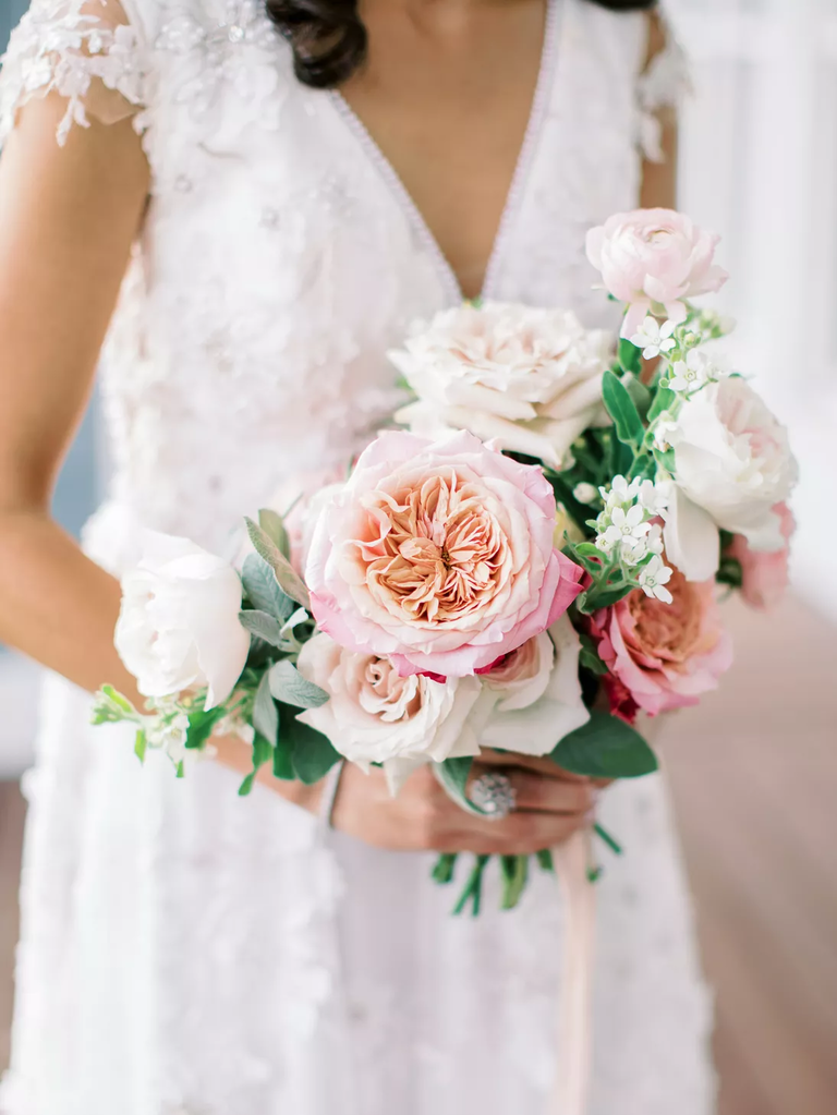 A bride holds a bouquet bursting with flowers of white and pale pink.