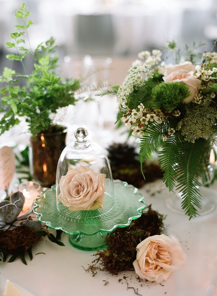 Single roses were displayed on green sea-glass cake stands under clear-glass terrariums. Green trick dianthus, wildflowers, ferns and moss added a rustic woodland feel.
