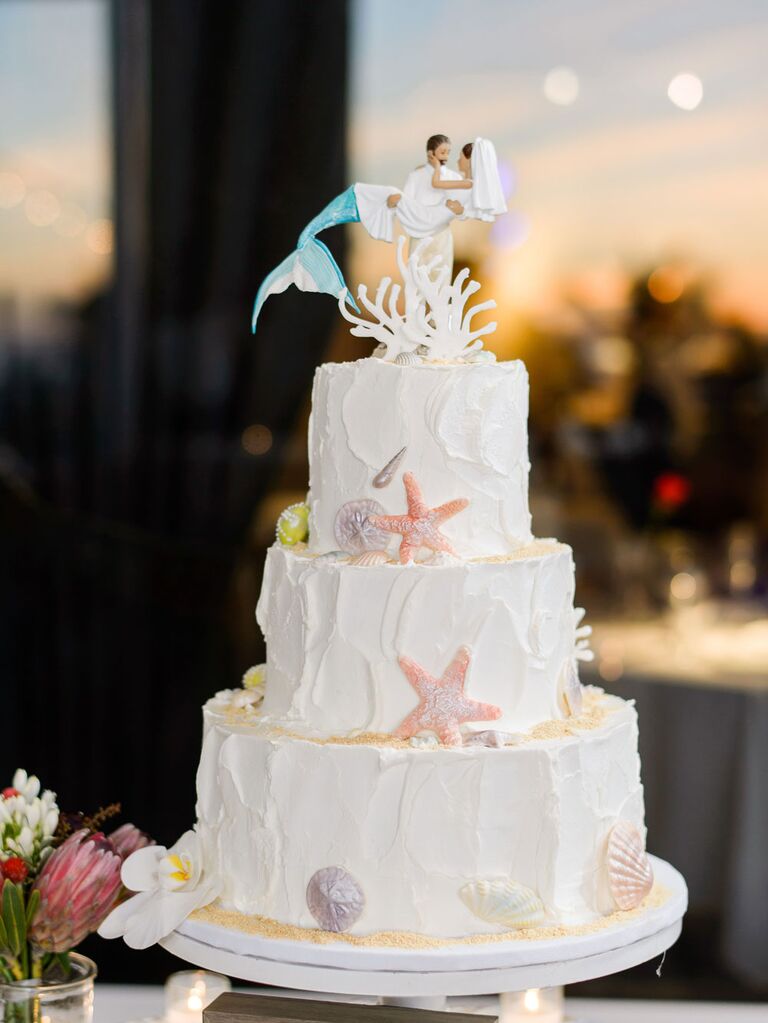 White beach-themed wedding cake with custom mermaid cake topper
