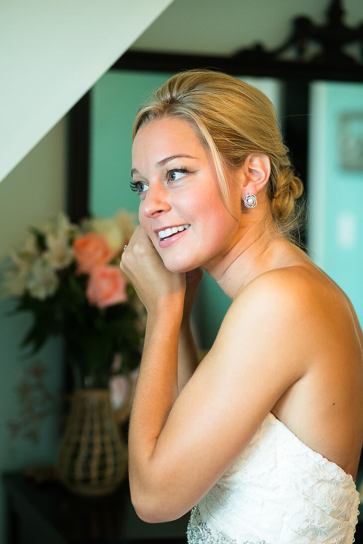 With a little help from the team at Head Games, Caitlin wore her hair in a classic updo with a few loose strands for a romantic touch. It was just the right fit for her all-lace white wedding dress by Mikaella Bridal. She finished off the look with bold pearl earrings surrounded by a fun curved halo design and simple espadrilles with white bows.
