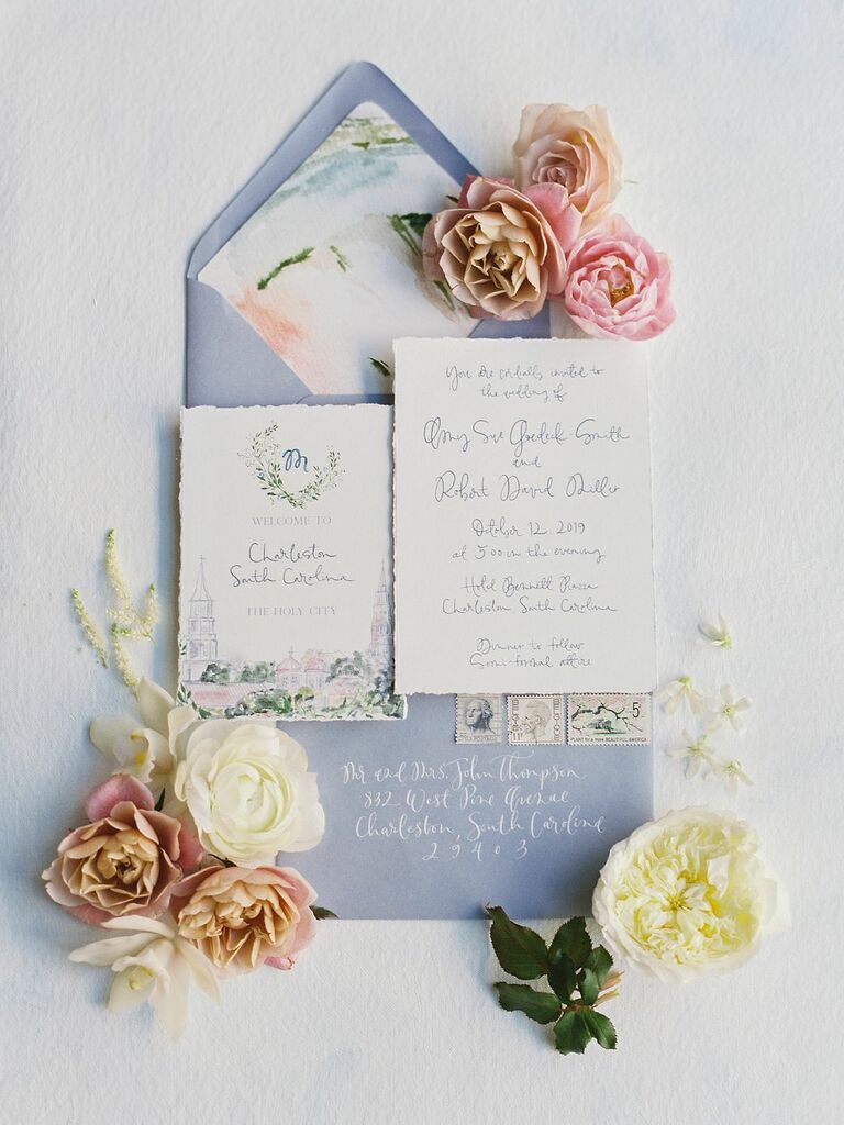 styled flat lay of light blue wedding invitation suite with watercolor crest, floral envelope liner and calligraphy