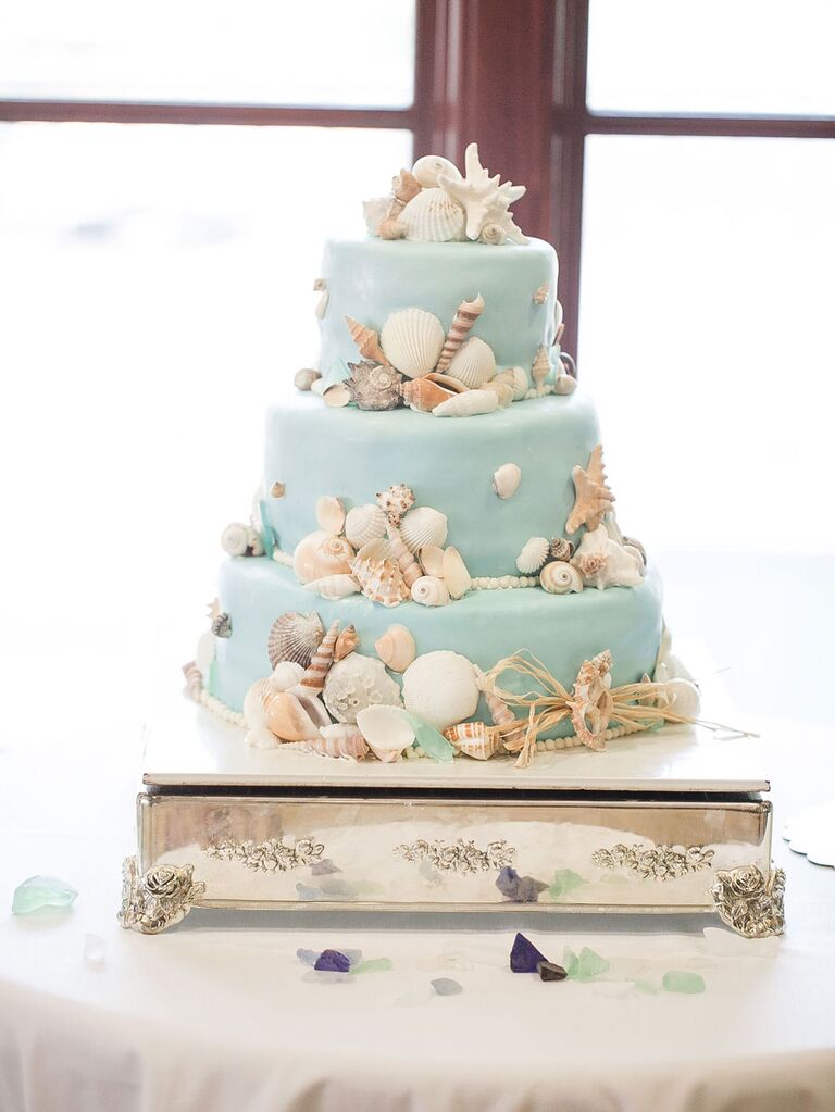 Three-tier light blue beach-themed wedding cake with seashells and starfish