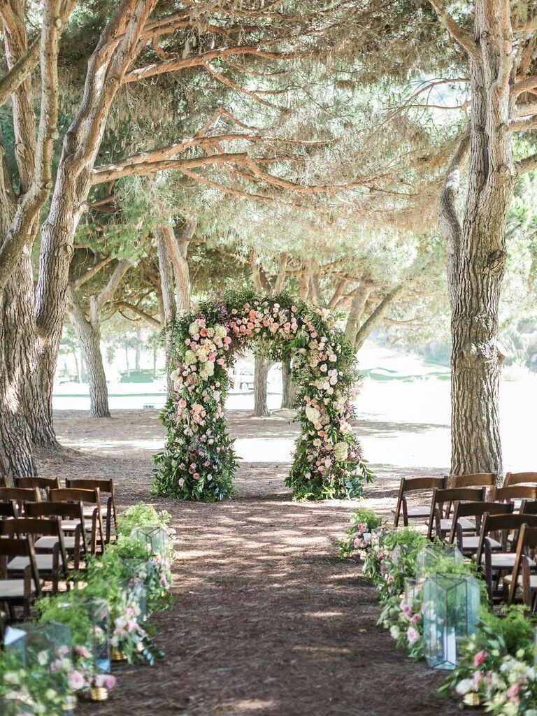 outdoor wedding ceremony in wooded area with floral and greenery arch at the altar