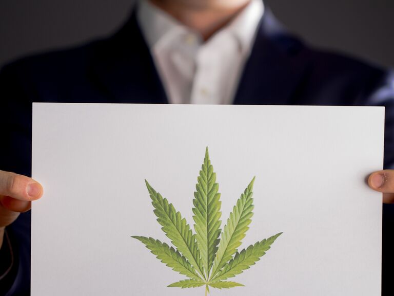 Person holding a piece a paper with a marijuana leaf on it.