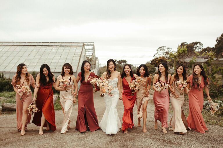 bride walks with her bridesmaids wearing mix-and-match rust orange and pink bridesmaid dresses 