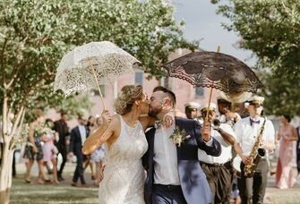 Newlyweds share a sweet kiss while holding fashionable lace parasols. 