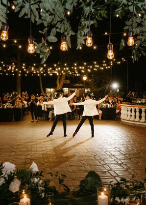 Grooms in Matching Formal Attire Doing Choreographed First Dance Under String Lights, Hanging Greenery