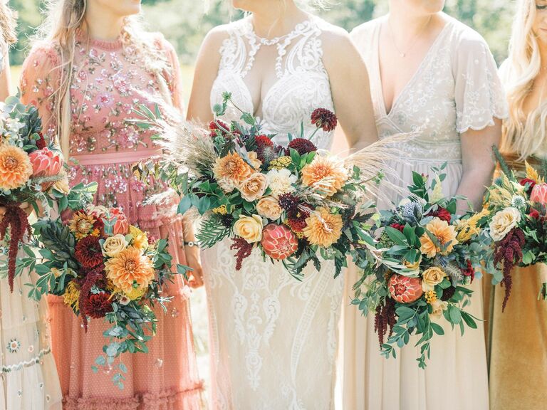 Bride and bridesmaids hold bouquets of orange and yellow dahlias. 