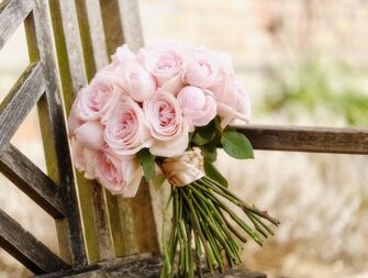 A pale pink bouquet sits propped, alone, against the back of a rustic wooden chair.