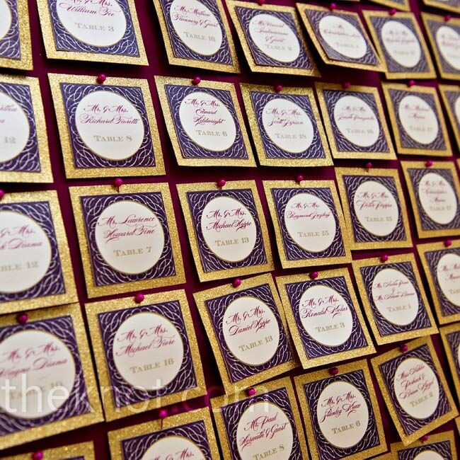 Purple and gold glittered escort cards were displayed on a fabric-covered board.