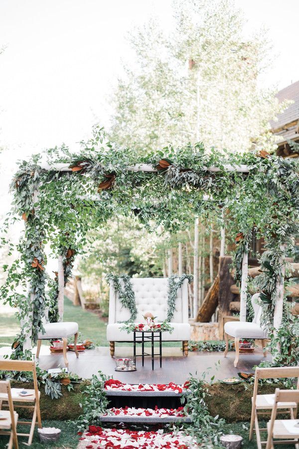 Greenery covered mandap with upholstered chair underneath