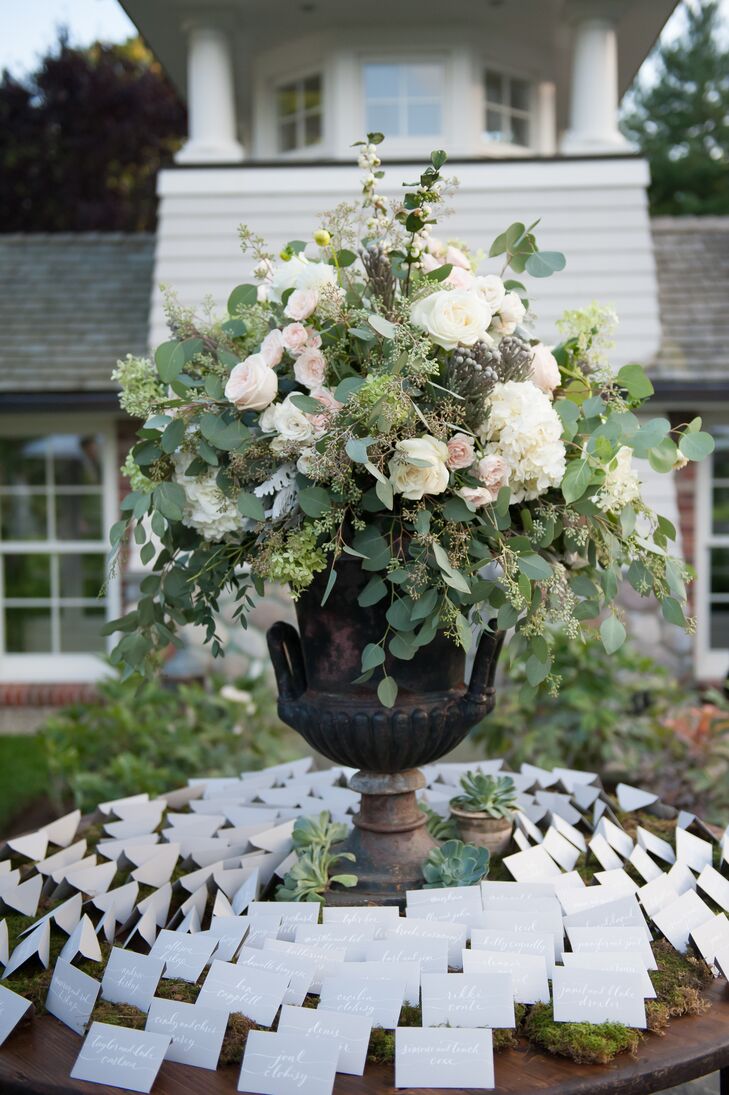 Dragonfly Events left no detail overlooked, creating sophisticated, statement-making arrangements of eucalyptus, roses, hydrangeas and ranunculus displayed in stately stone urns for the escort-card table and ceremony aisles.