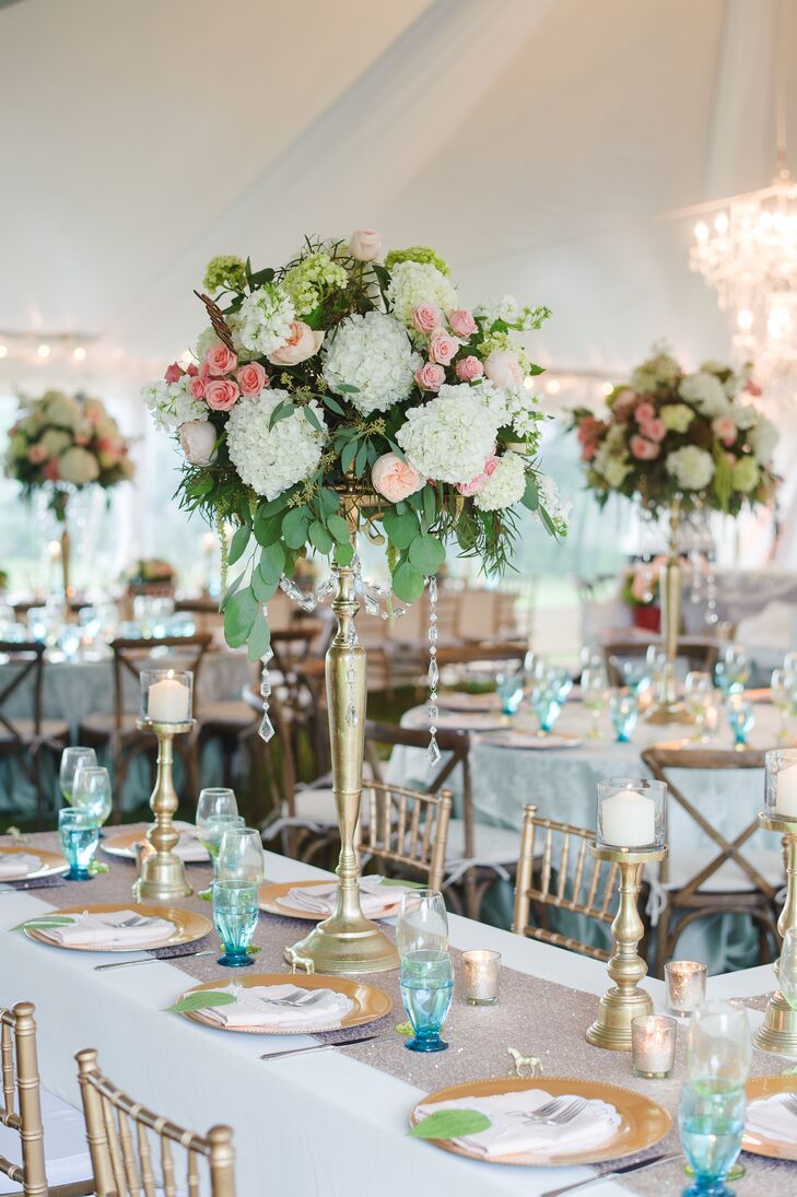 The couple decorated their reception in shades of gold, blue and white. Some of Erica and Cole’s family style tables were decorated with tall arrangements of blush garden roses, white and green hydrangea, pink roses and eucalyptus atop a gold stand. Crystal accents were hung from each arrangement.