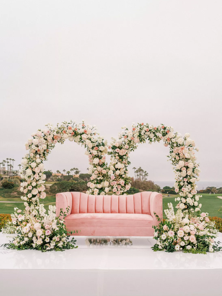 A blush pink sofa sits beneath a pair of romantic floral arches.