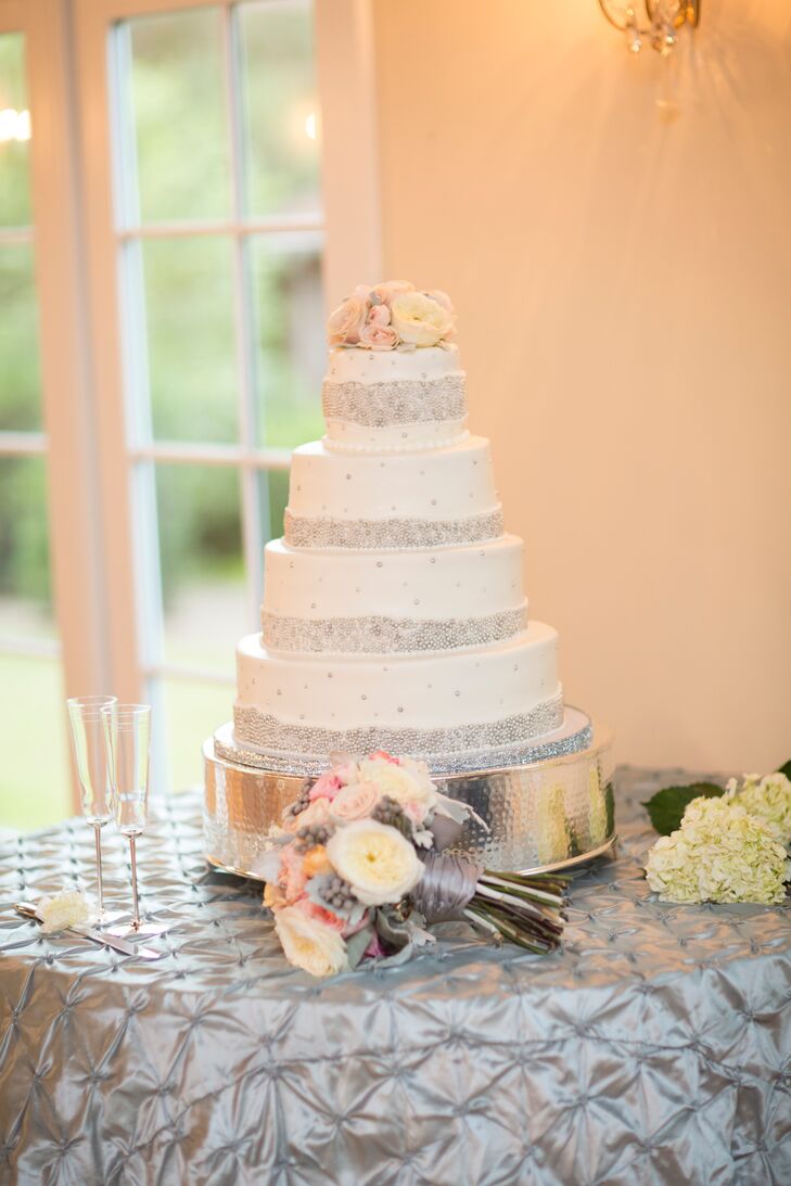 The white wedding cake was decorated with bands of silver dragees as well as pink roses and white ranunculuses.