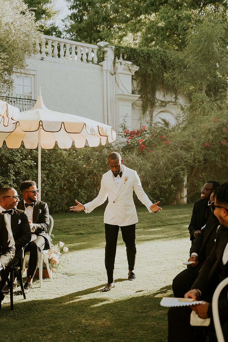 Groom in White Tuxedo Jacket and Black Pants Walking Down the Lawn Aisle, Umbrellas