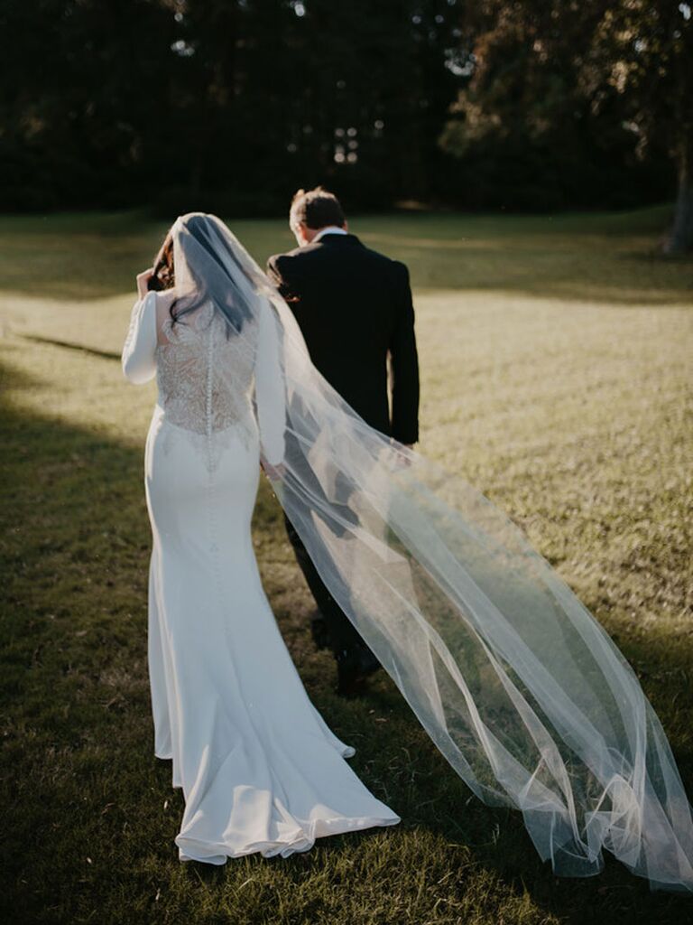 Groom and bride walking on wedding day with veil trailing in the wind