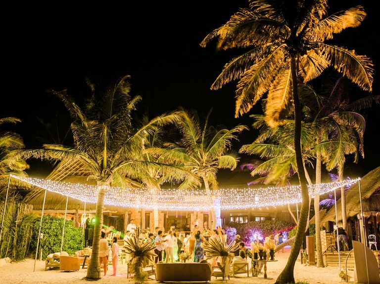 outdoor wedding reception at beach venue with a canopy of string lights hanging from palm trees above the dance floor