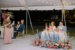 Bride and Groom at Sweetheart Table With Floor Flowers Watching Maid of Honor Speech