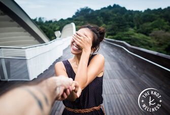 smiling woman holding man's hand and covering her eyes with her hand