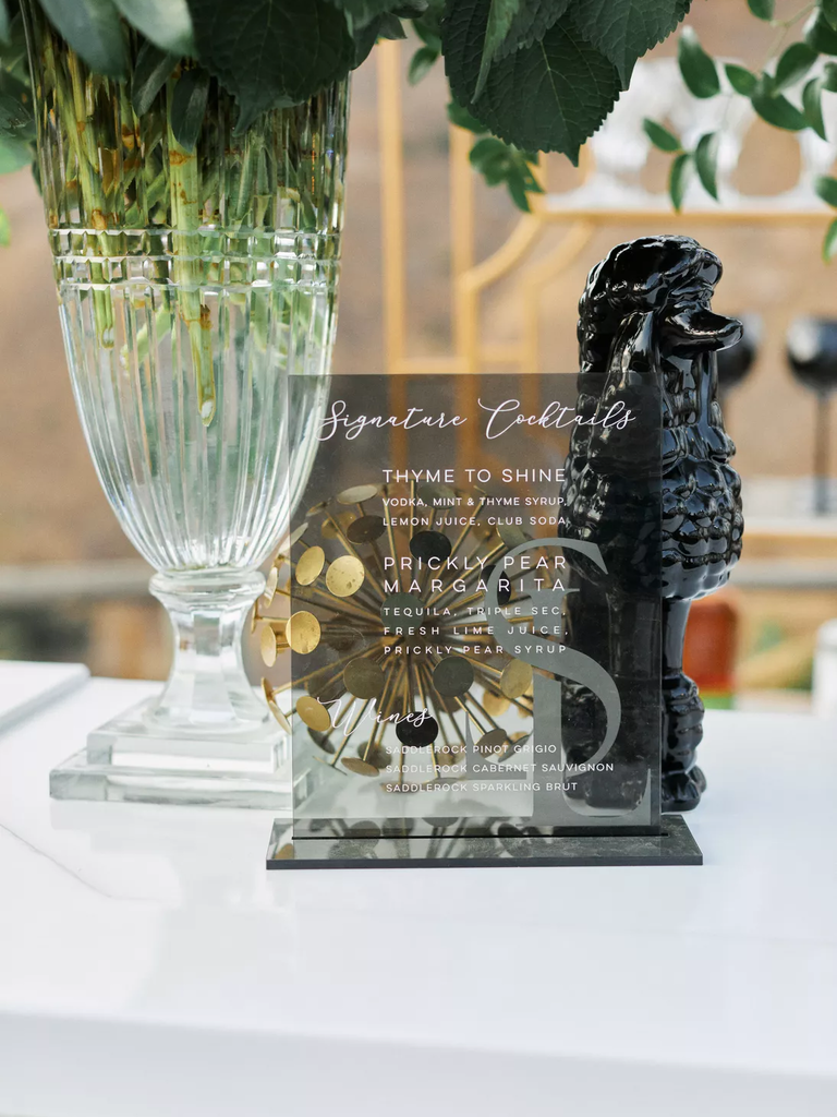 A glass cocktail menu sat beside a floral arrangement.
