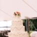 The four-tiered ivory wedding cake was placed on top a gold metal cake stand and was decorated with gold accents. On the top of the cake was a small arrangement of pink roses.