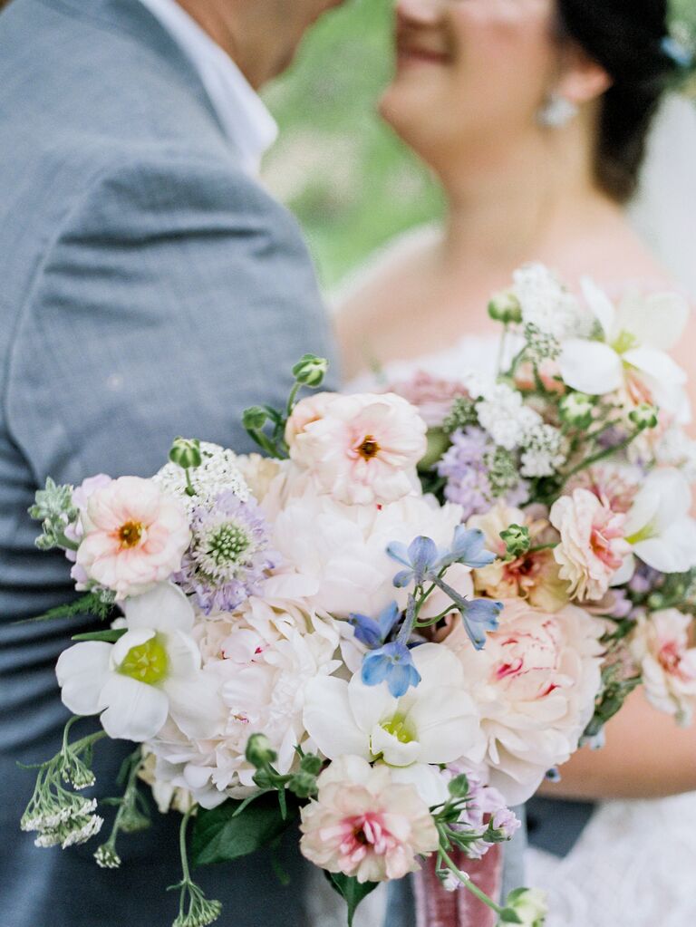 close up of bride holding pastel wedding bouquet with blue delphinium, pink cosmos, pink peonies, purple scabiosa and queen annes lace