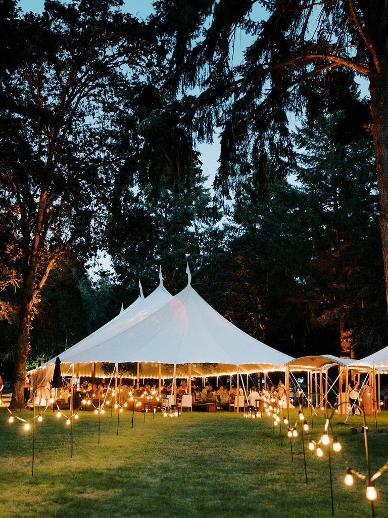 sperry wedding reception tent with bistro string lights on hooks lining the pathway across the grass