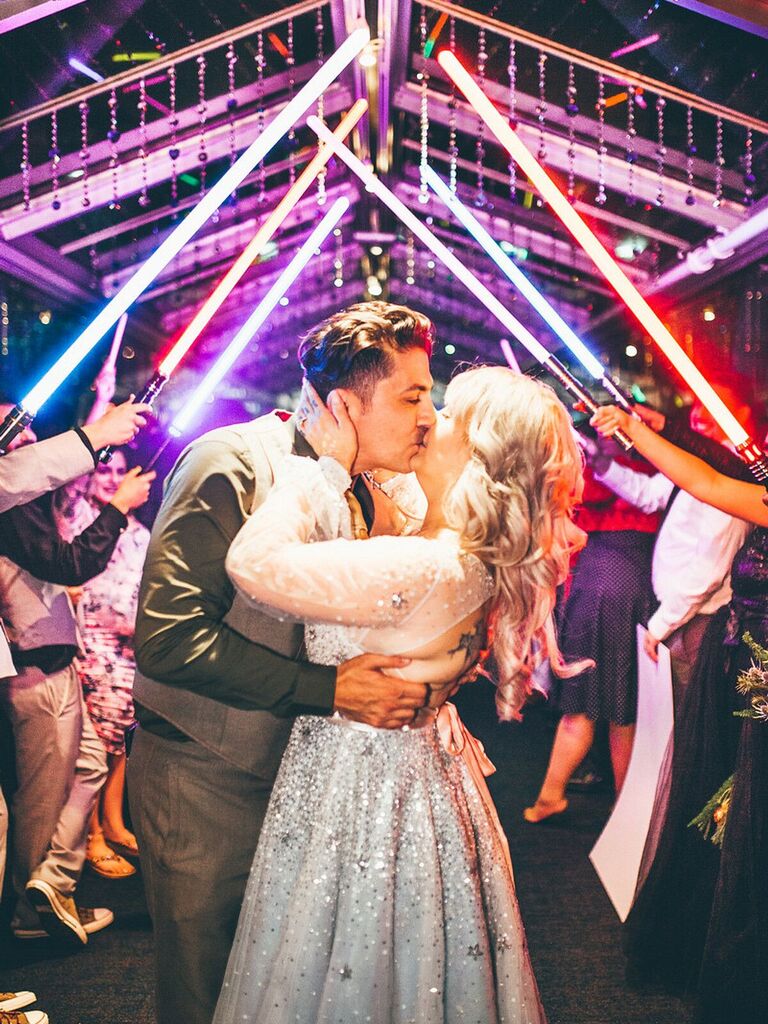 Bride and groom kiss under lightsaber arch.