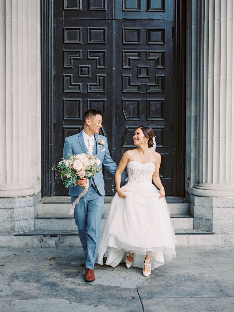 bride smiles and walks next to groom wearing light blue suit