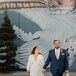 Bride in Retro Sequin Dress With V-Neckline and Groom in Blue Suit Walking With Small Dog