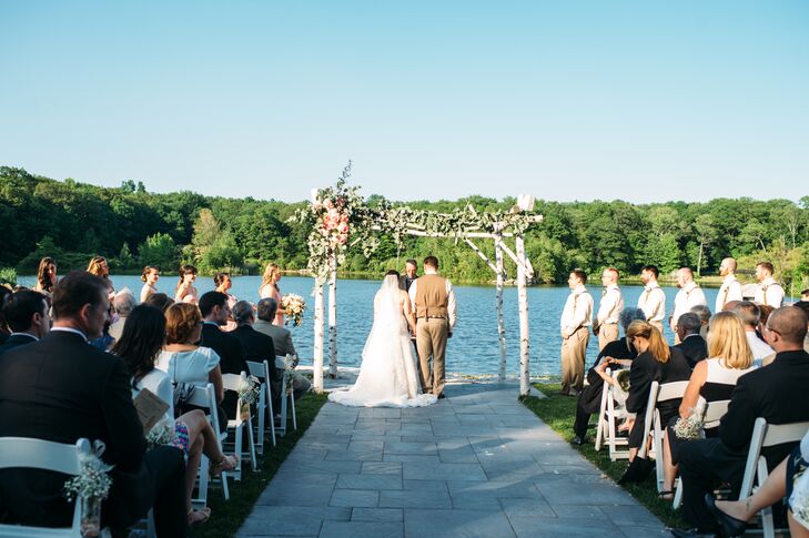 Baby’s breath marked every row of white folding chairs toward their romantic eucalyptus and rose-covered wedding arbor at Rock Island Lake Club in Sparta, New Jersey. As they stood below it, the couple took part in an ultra-personalized ceremony. “The ceremony was done by a great family friend and second father practically, Glenn Craig,” Kim says. Their friends and family members also assisted in the service with two spoken Bible readings and poems.
