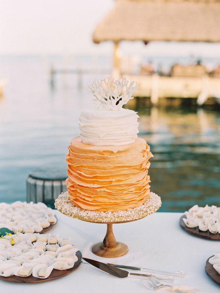 Orange and white ruffled beach wedding cake with coral topper
