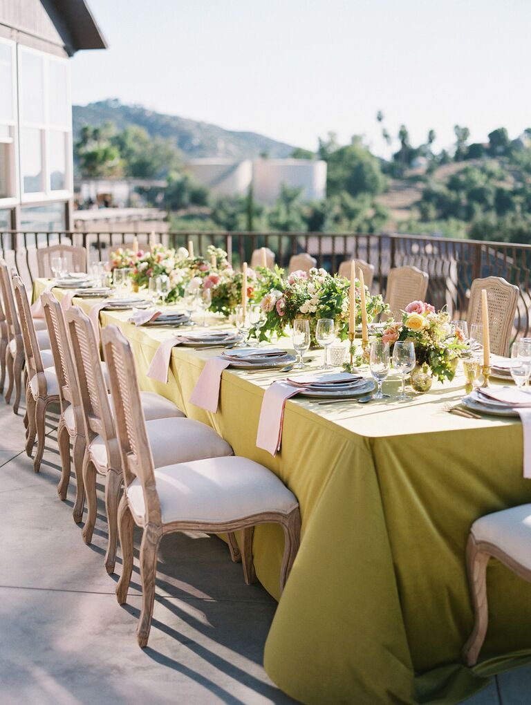 example of 2022 wedding color trend outdoor wedding reception tablescape with moss green tablecloth and wooden upholstered chairs
