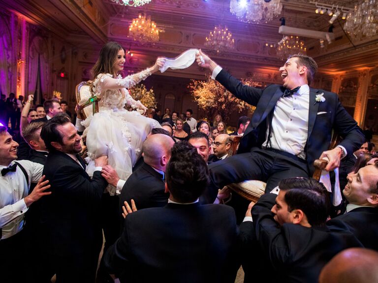 Bride and groom lifted in chairs by groomsmen during traditional Hora