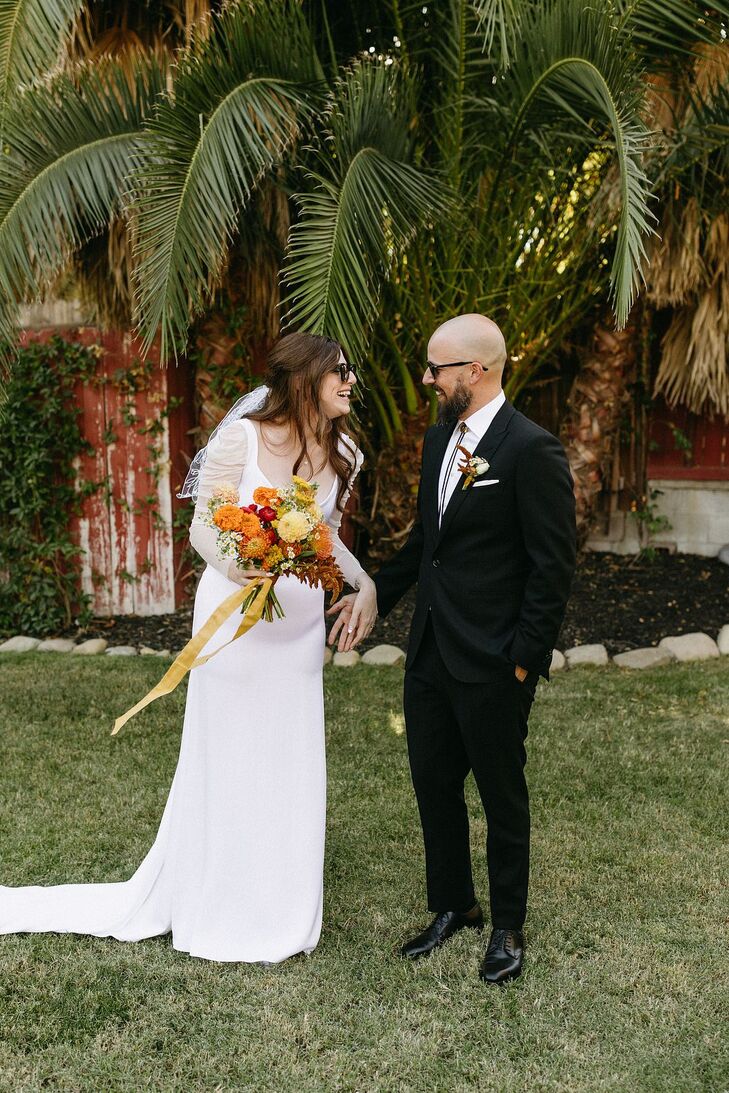 Bride in Modern Wedding Gown With Orange, Red Bouquet and Groom in Suit With Sunglasses