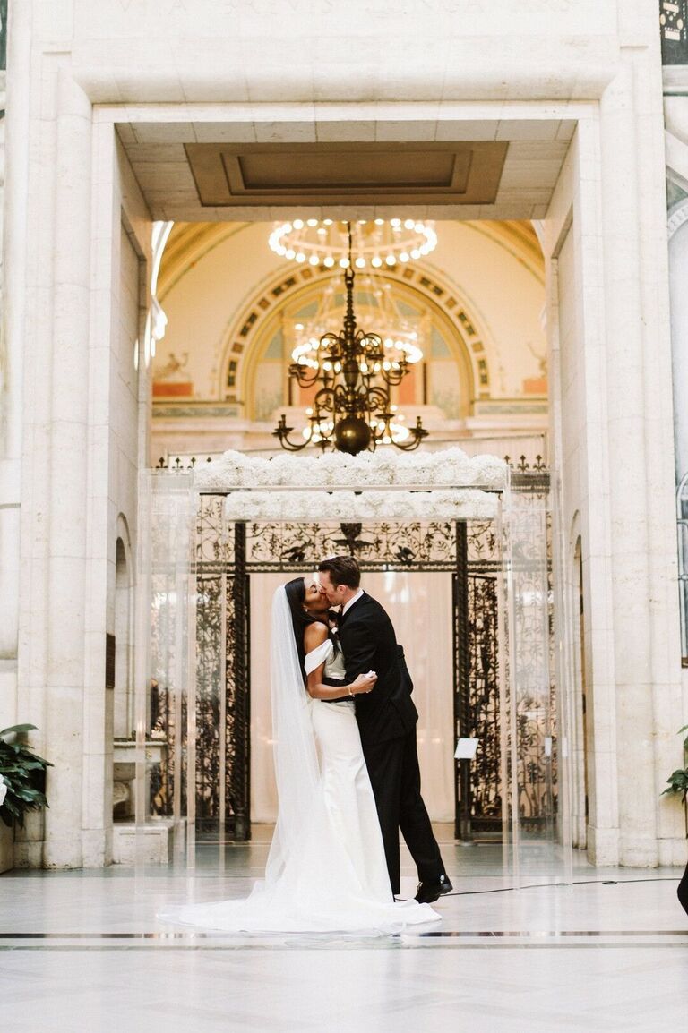 Ceremony first kiss in front of acrylic arch with white flowers
