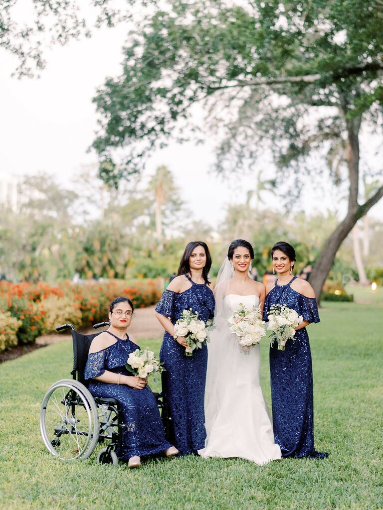 bride stands with bridesmaids wearing long sequin navy blue dresses