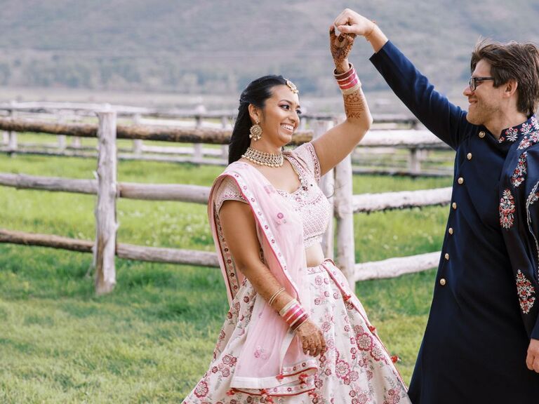 Couple in Indian wedding attire dancing in rustic field