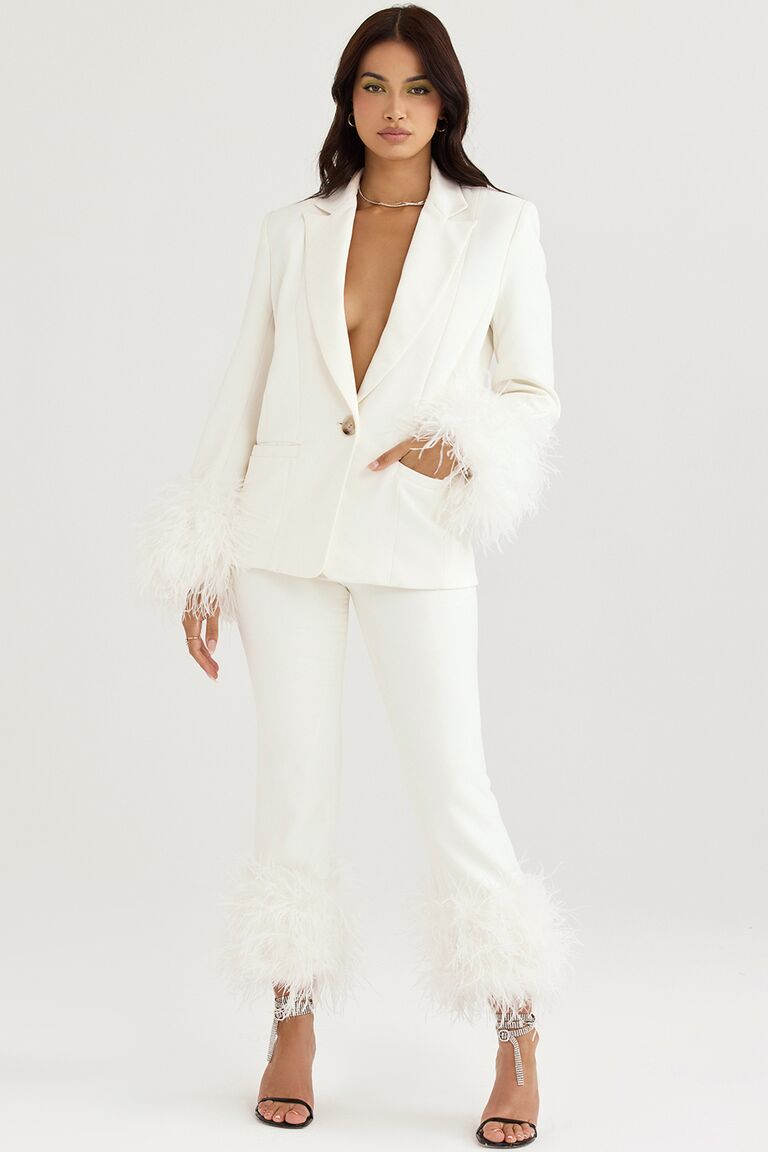 Model wears a white pantsuit with feather trim. 